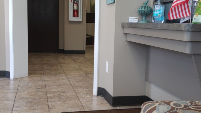 Interior reception area with tiled flooring, beige walls, doorway entry, counter desk, and waiting seating with television