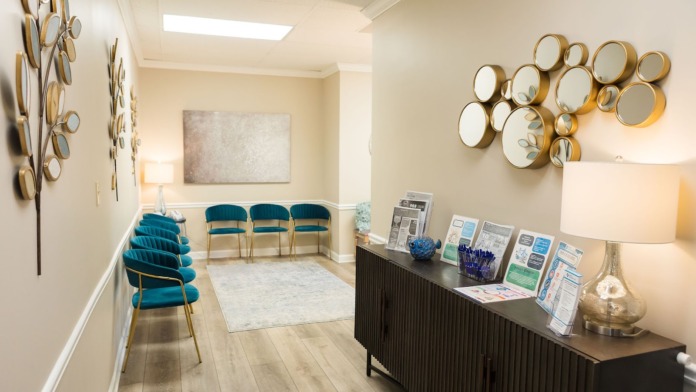 Interior reception space with decorative mirrors, blue cushioned seating, beige walls, and black reception desk with brochures