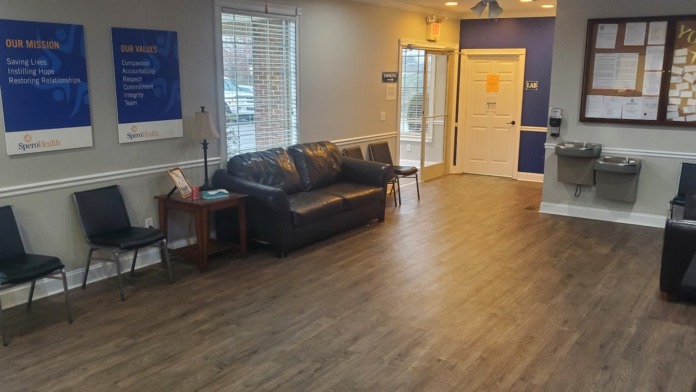 Interior reception area with mission statement signage, seating, wood flooring, and administrative workspace.