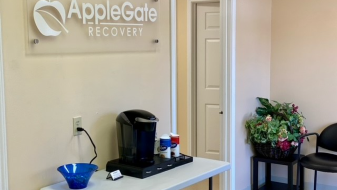 Interior reception area with AppleGate Recovery sign, beverage station, flowers, and doorway leading to facility interior