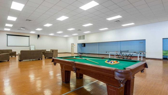 Interior recreation room with pool tables, ping pong table, brown seating furniture, projection screen, and hardwood flooring