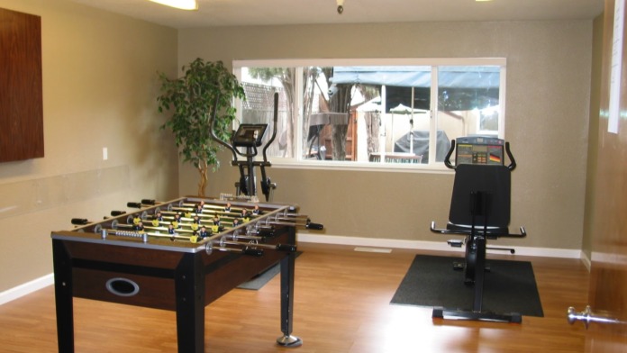 Interior recreation room featuring foosball table, stationary bikes, treadmill, and large windows overlooking outdoor patio area