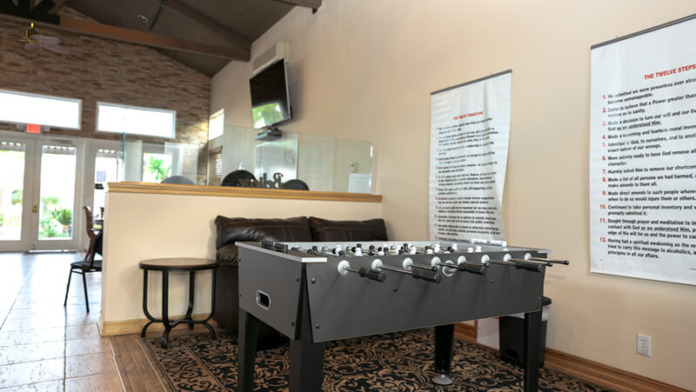 Interior recreational space with foosball table, treatment information poster on wall, and natural lighting from entrance area