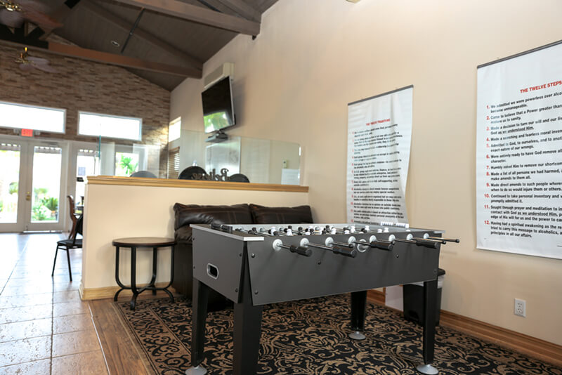 Interior recreational space with foosball table, treatment information poster on wall, and natural lighting from entrance area