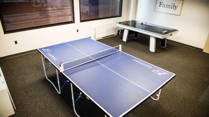 Interior recreation room with ping pong tables, air hockey table, windows with blinds, and activity signage