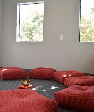Interior relaxation space with red cushioned seating elements arranged on dark floor with large windows for natural light