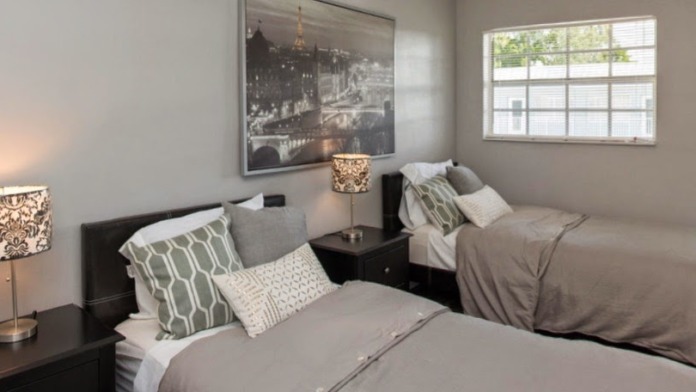 Interior residential unit with open kitchen, wood cabinetry, stainless steel appliances, living area with sofa, and balcony access with palm view