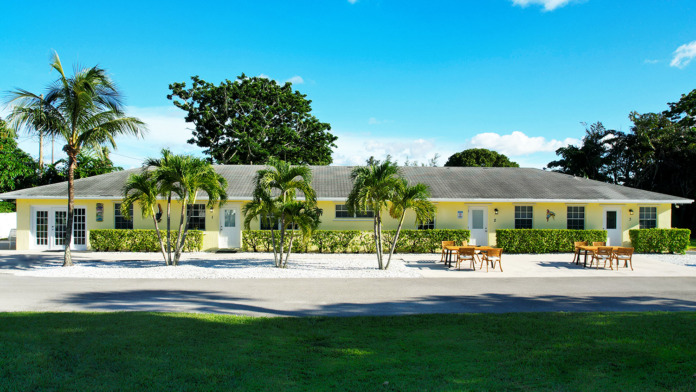 Exterior yellow and white residential treatment building with multiple units, green landscaping, palm trees, and outdoor seating