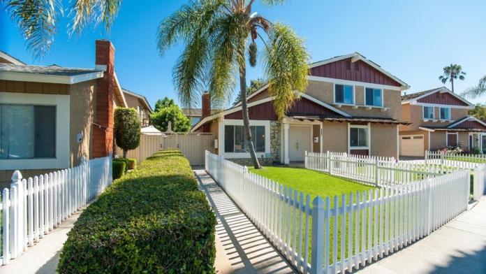 Exterior view of residential properties with white picket fencing, landscaping, and palm trees lining the street