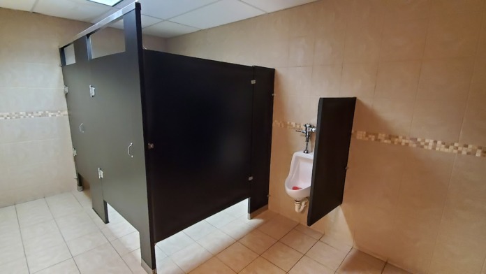 Interior bathroom showing multiple stall compartments with privacy doors and wall-mounted fixtures and dispensers