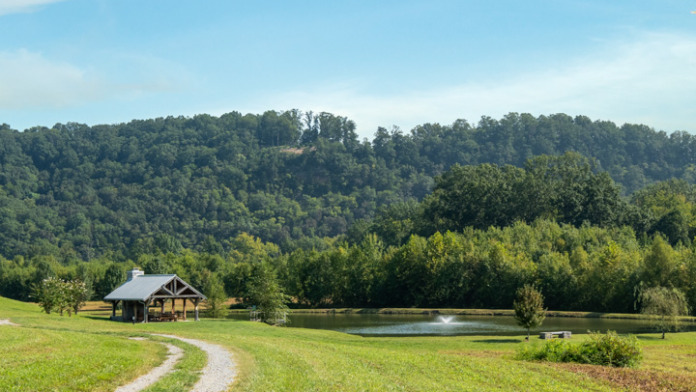 Exterior showing riverside pavilion, gravel pathway, manicured lawn, mature trees, and wooded landscape