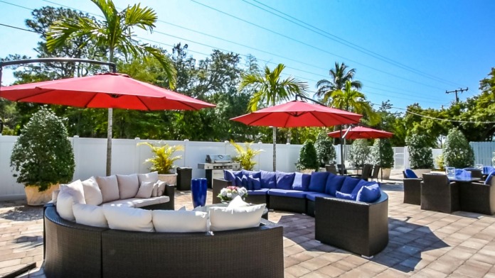 Outdoor rooftop terrace with red umbrellas, curved lounge furniture with cushions, palm trees, white privacy fence, and facility buildings
