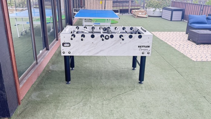 Outdoor rooftop space with recreational games, lounge seating, potted plants, and city views.