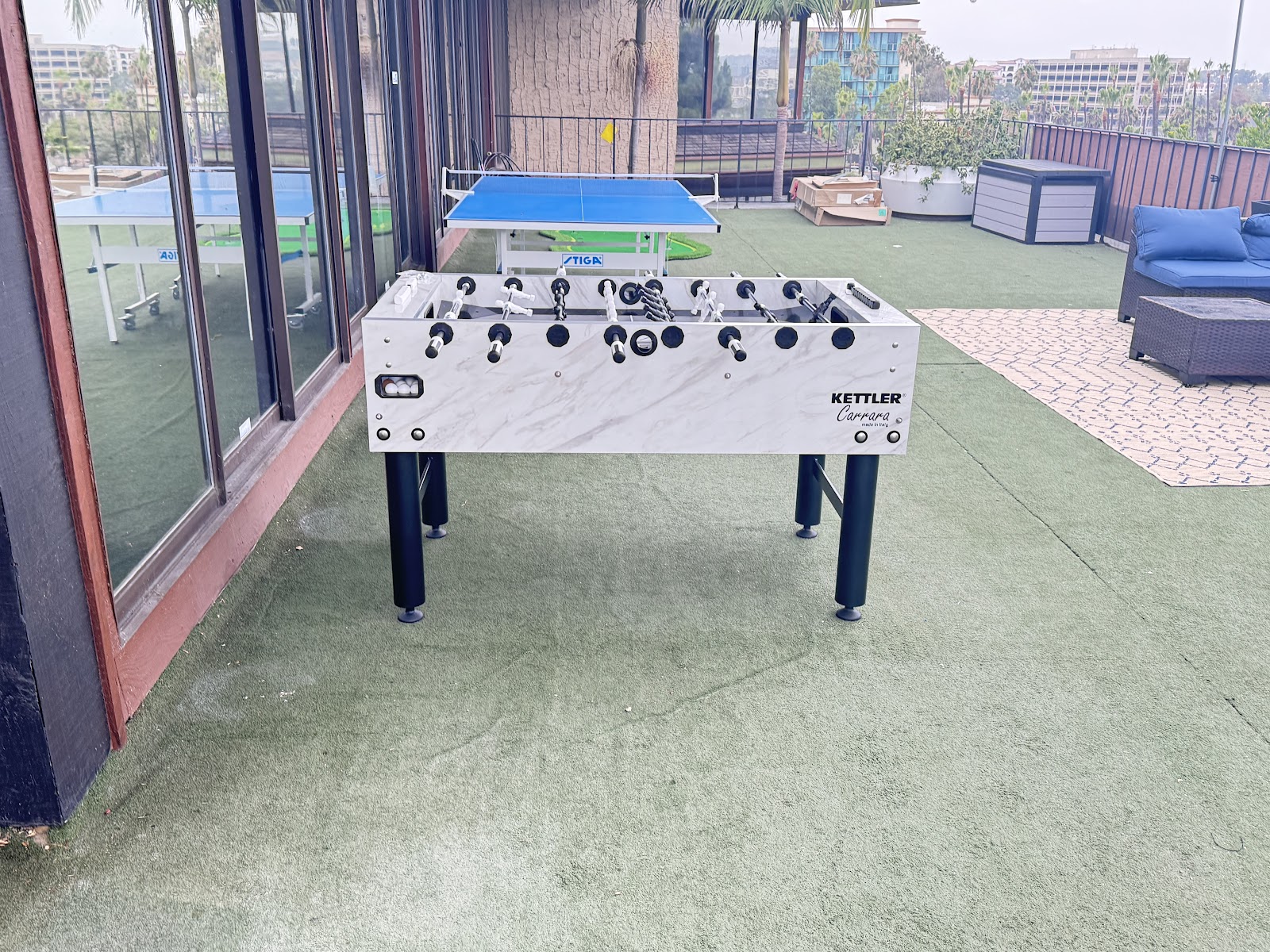 Outdoor rooftop space with recreational games, lounge seating, potted plants, and city views.