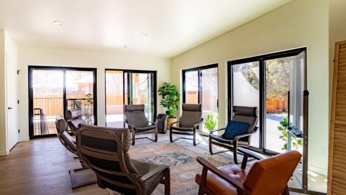 Interior sunlit lounge with multiple leather recliners, plants, patio doors opening to mountain views and deck area