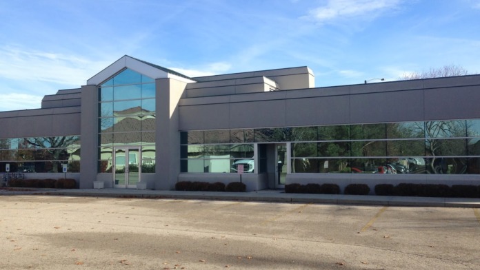 Exterior view of treatment facility building with modern glass windows, gray and white exterior, minimal landscaping, clear sky
