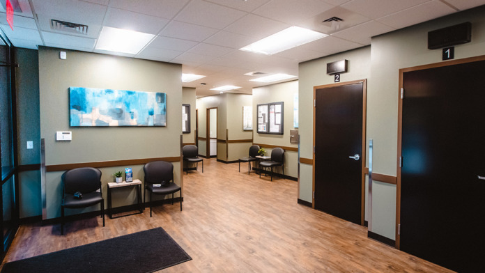 Interior narrow hallway with seating chairs, reception window, informational signage, and windows