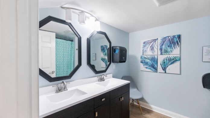 Interior bathroom with dual vanity sinks, black cabinetry, decorative octagonal mirrors, botanical wall art, and modern fixtures