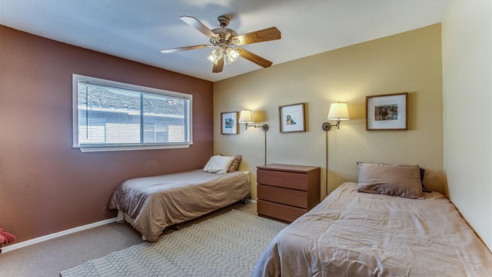 Interior patient bedroom with two twin beds, nightstands, ceiling fan, large window with natural light, and comfortable furnishings