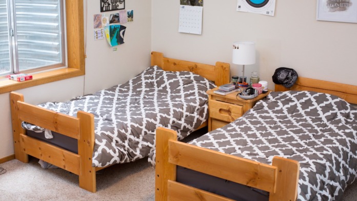 Interior residential bedroom with two wooden bed frames, patterned bedding, window with natural light, desk area, and wall decorations