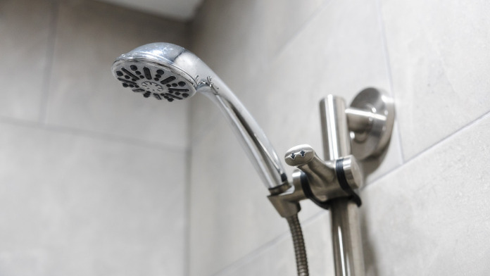Interior closeup of chrome shower showerhead and wall-mounted controls in bathroom with tile surround
