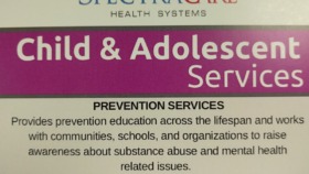Interior informational sign displaying SpectraCare Health Systems branding, mission statement, and service descriptions for child and adolescent prevention and court liaison programs