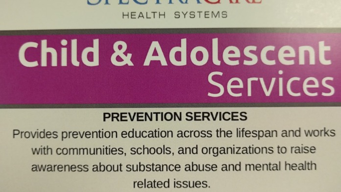 Interior informational sign displaying SpectraCare Health Systems branding, mission statement, and service descriptions for child and adolescent prevention and court liaison programs