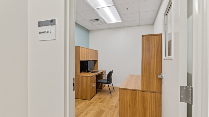Interior staff office with wooden desk and cabinetry, computer workstation, blue office chairs, and yellow-green accent wall