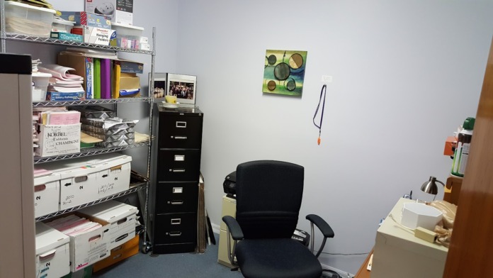 Interior office space with filing cabinets, shelving units with supplies, desk area, and wall decoration