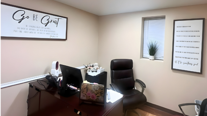 Interior office space with desk, computer, office chairs, wall-mounted motivational messages, and small accent table with plant