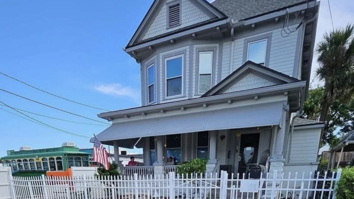 Exterior street view of Victorian treatment facility with front porch, railings, and adjacent properties visible.