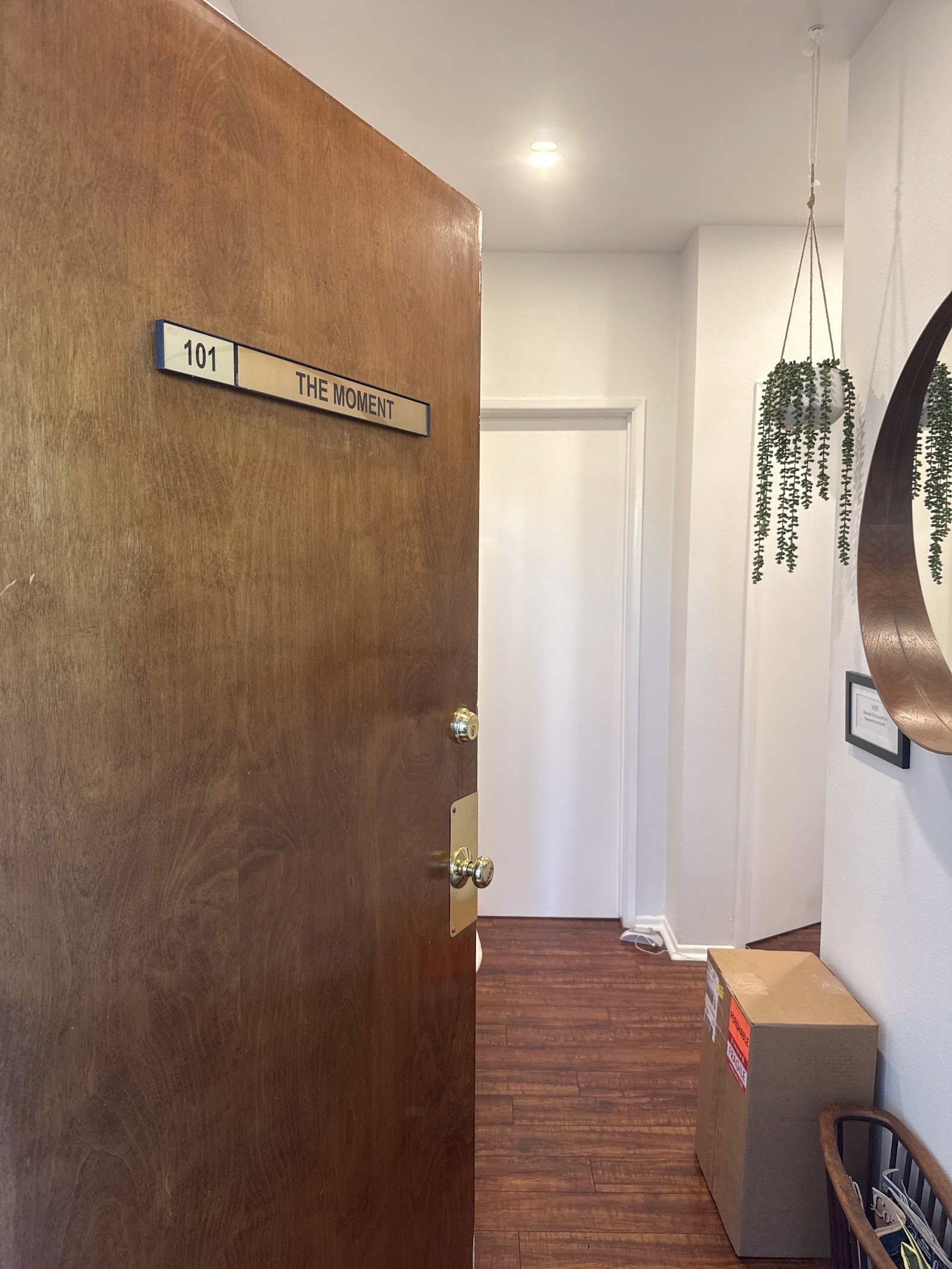 Interior hallway showing Suite 101 entrance door with The Moment Health signage, hanging plants, and wood flooring