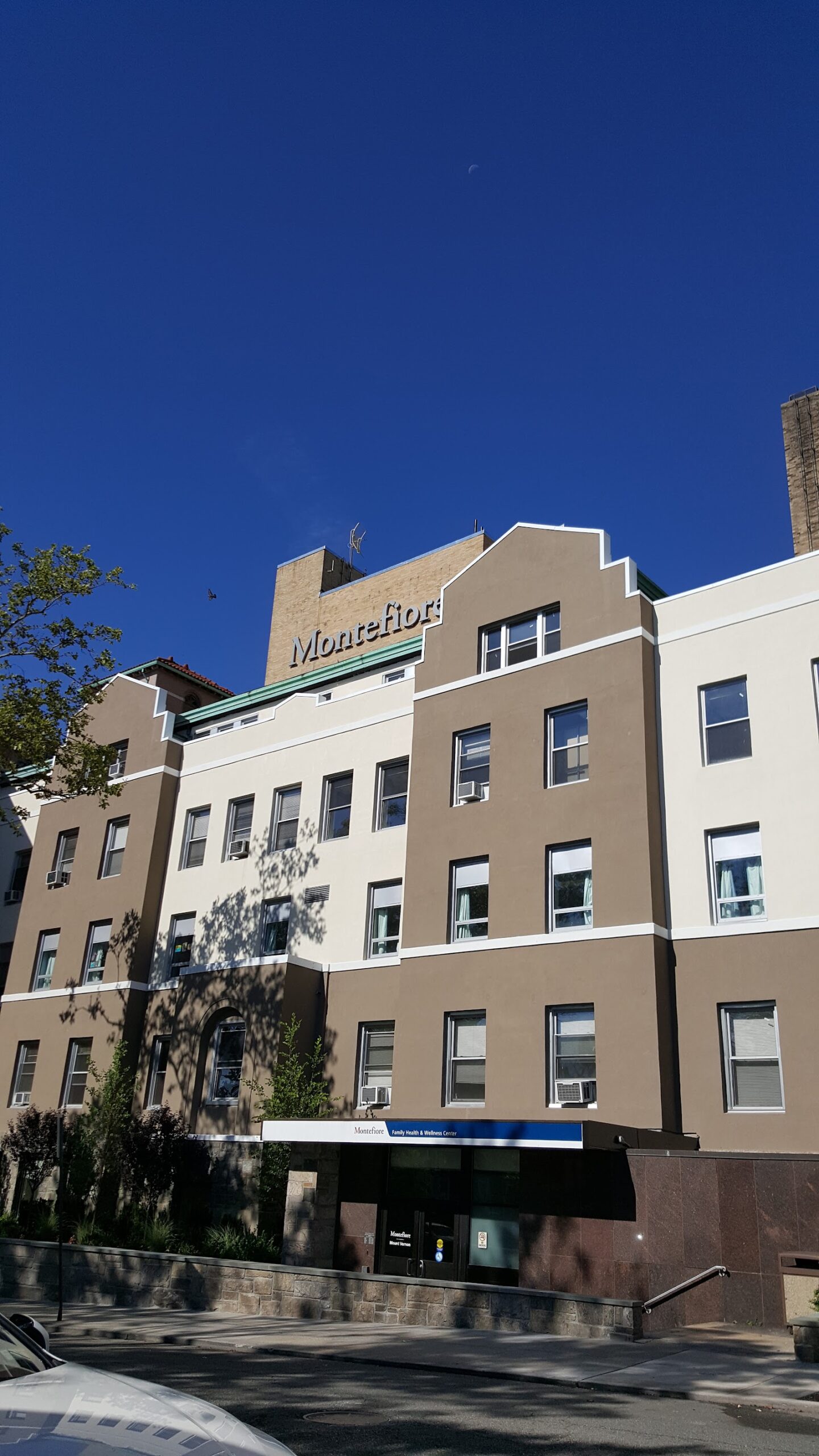 Exterior tall multi-story tan and white hospital building with Montefiore roofline signage and street-level storefront entrance