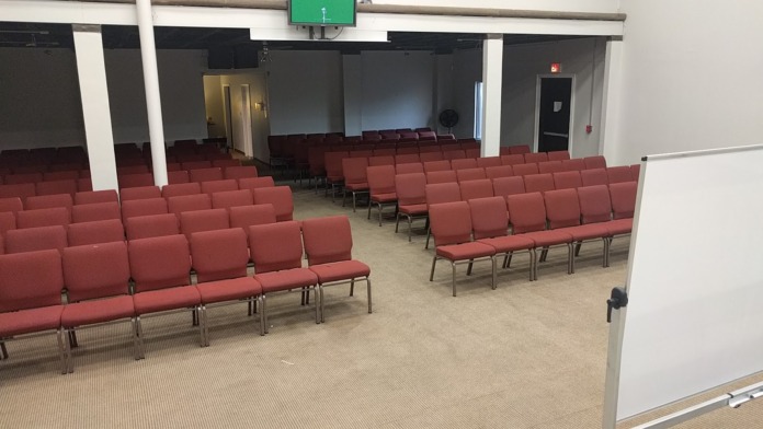 Interior auditorium with burgundy padded seating rows, stage area with black backdrop, and white support columns