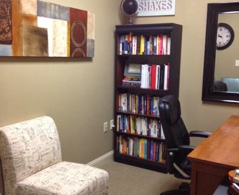 Interior office space with upholstered chair, bookshelf with books and decor, motivational wall signage, and desk area