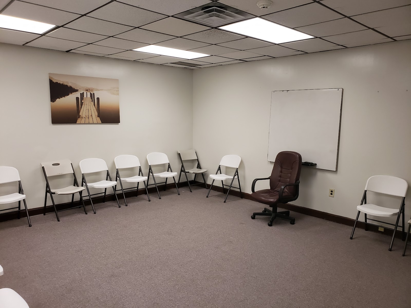 Interior room with semicircular chair arrangement, office chair, whiteboard, landscape wall art, and drop ceiling lighting