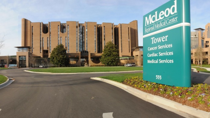 Tan brick medical building with modern curved architecture and blue directional sign indicating tower and services