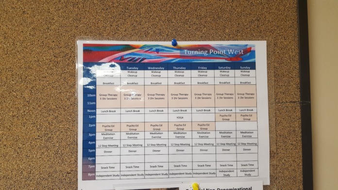 Interior wall posting showing Turning Point West daily schedule with times for group therapy, meals, and activities