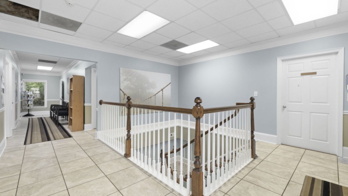 Interior hallway with white railings, wooden banister, light blue and cream walls, tile flooring, and multiple doors