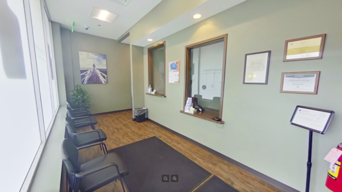Interior waiting area with rows of black chairs, windows with white curtains, green walls, and framed certifications