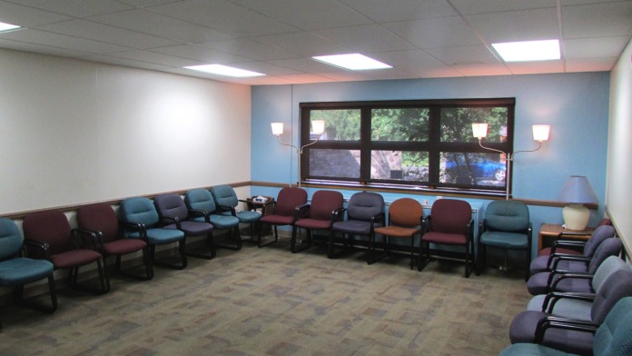 Interior waiting area with arranged upholstered chairs in burgundy and teal, recessed lighting, and large windows.