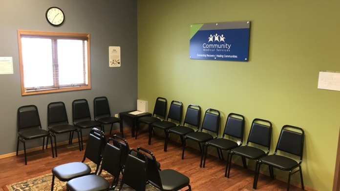 Interior waiting room with lime-green and gray walls, multiple black chairs, wall-mounted clock, and facility signage