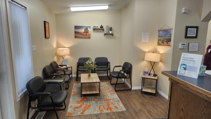 Interior waiting room with black chairs, coffee tables, landscape wall art, and ceiling fan with warm lighting