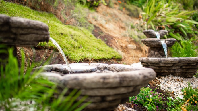 Outdoor tiered stone water fountains with cascading water, moss, and decorative landscape plantings.