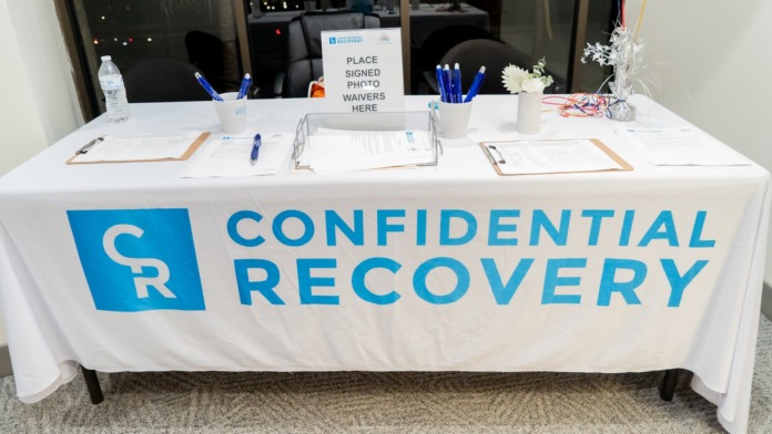 Interior reception display table with Confidential Recovery branding, signage, and waiver forms.