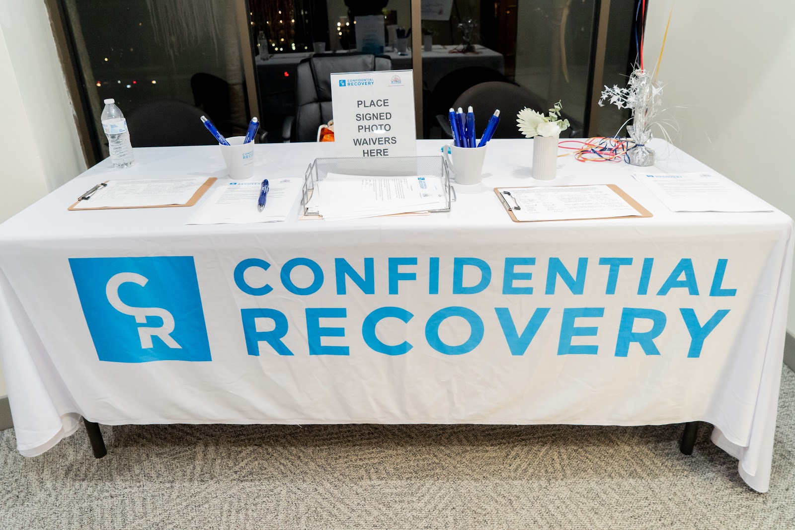 Interior reception display table with Confidential Recovery branding, signage, and waiver forms.