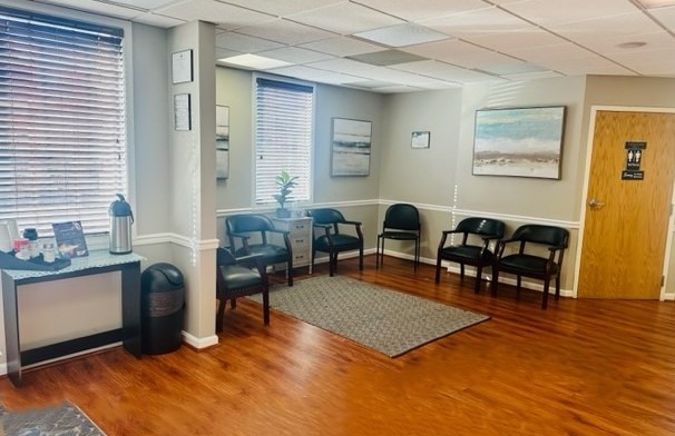 Interior waiting room with comfortable seating, hardwood flooring, large windows with natural light, and wall art