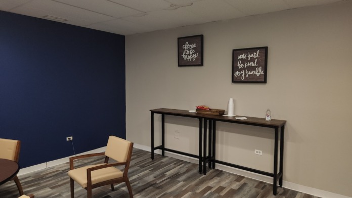 Interior room with tan chairs, dark navy accent wall, framed motivational quotes, and serving table with supplies