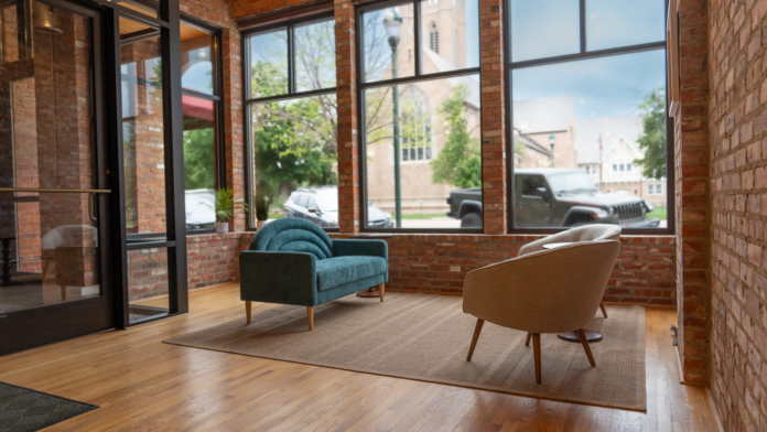 Interior seating area with large windows overlooking parking, mid-century modern chairs, and wood flooring