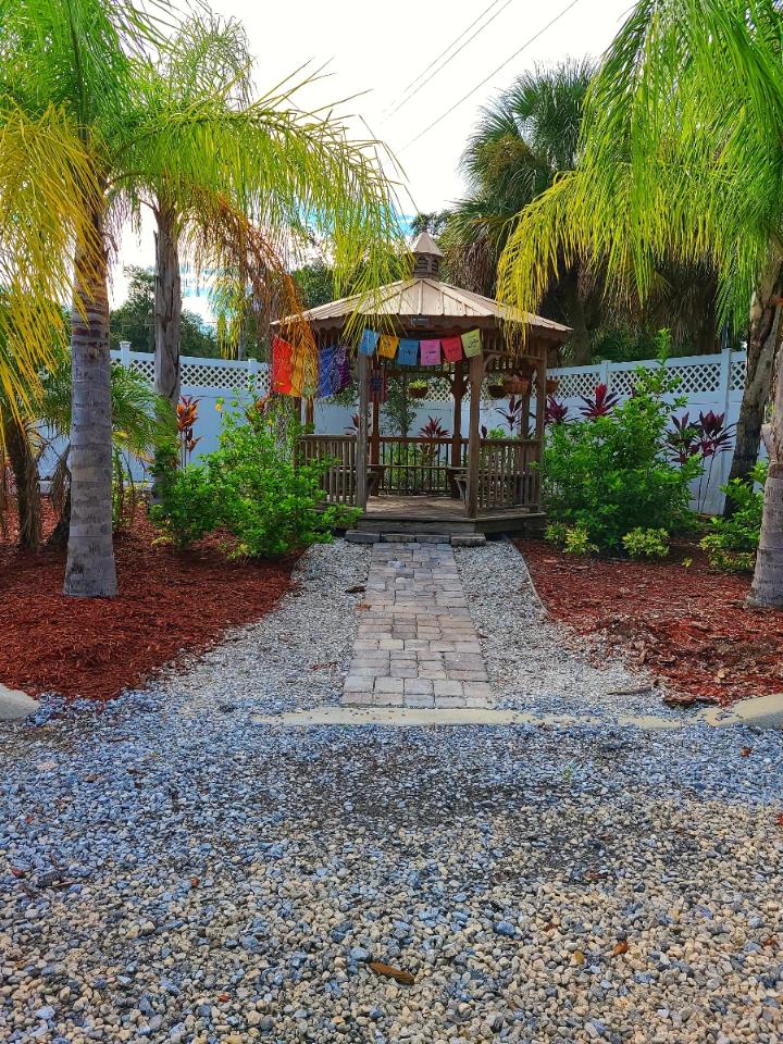 Exterior peaceful garden pathway leading to wooden gazebo with palm trees, decorative landscaping, and seating area